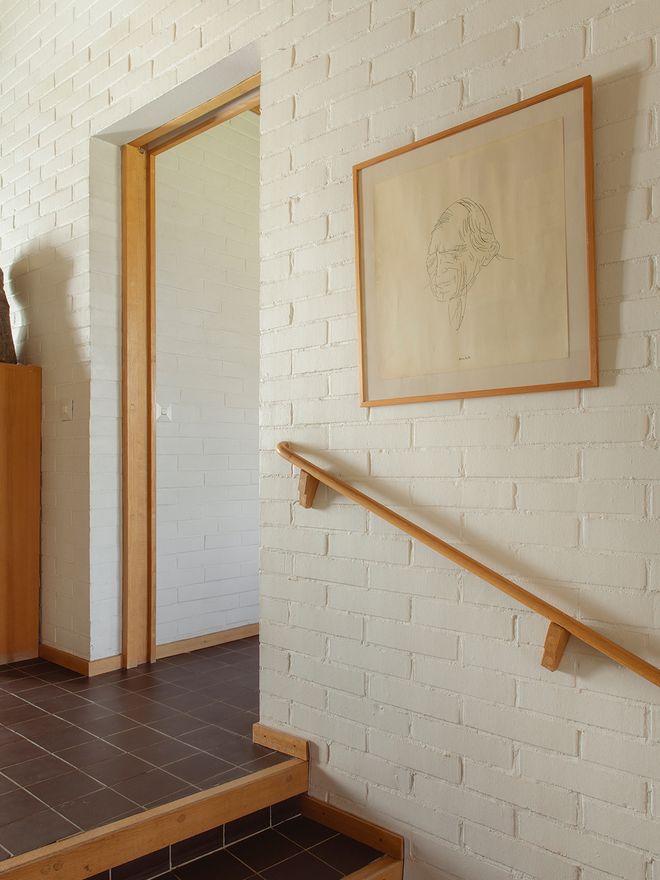 A hallway at Villa Skeppet with white painted brick walls, dark tile flooring, and a framed line-drawing portrait by Roberto Sambonet
