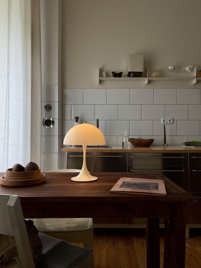 Louis Poulsen's liyt Panthella table lamp on a dark wooden table, with a white tiled wall and a kitchen shelf behind it.