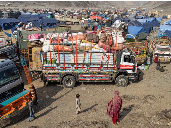A woman and child stand next to a fully loaded truck at the Torkham refugee camp