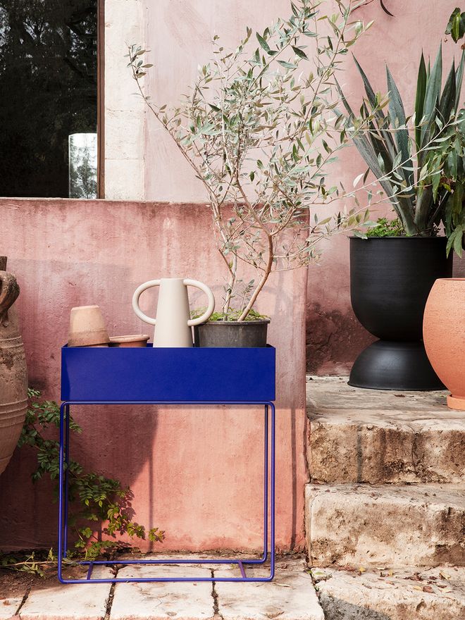 An image of Ferm Living's bright blue Plant Box in the garden, filled with pots and plants.