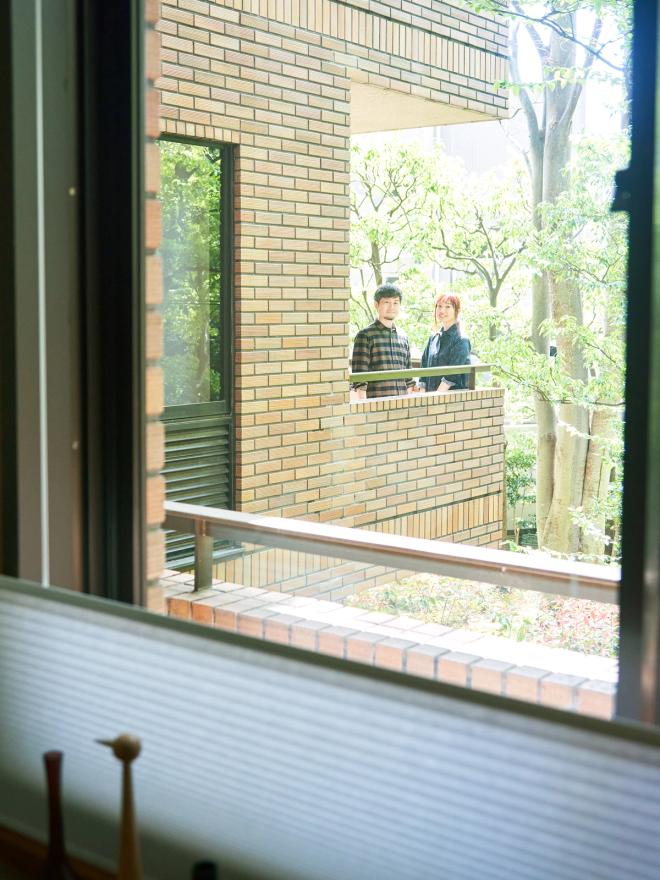 A view through a window to a balcony where two people are standing