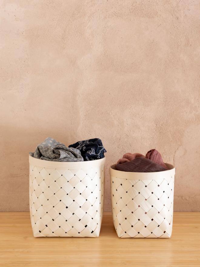 Two light woven storage baskets filled with folded textiles on a wooden floor.