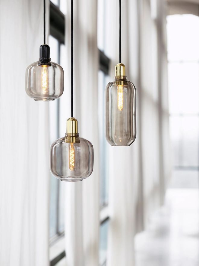 Three smoke-gray Amp pendant lights with spiral LED bulbs glowing inside, against white curtains.