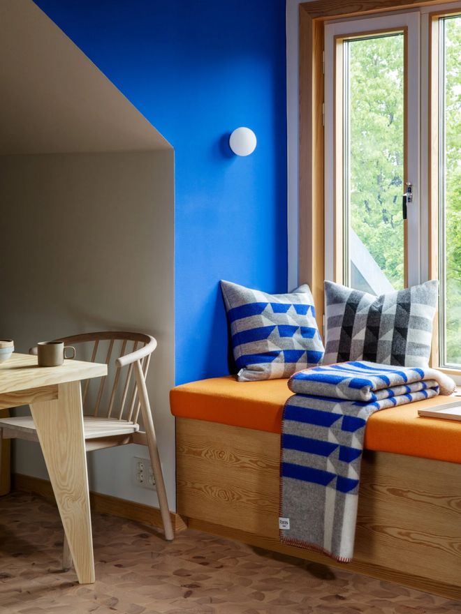 A blue-walled reading nook by a kitchen window with Røros Tweed’s Kvam throw and cushions