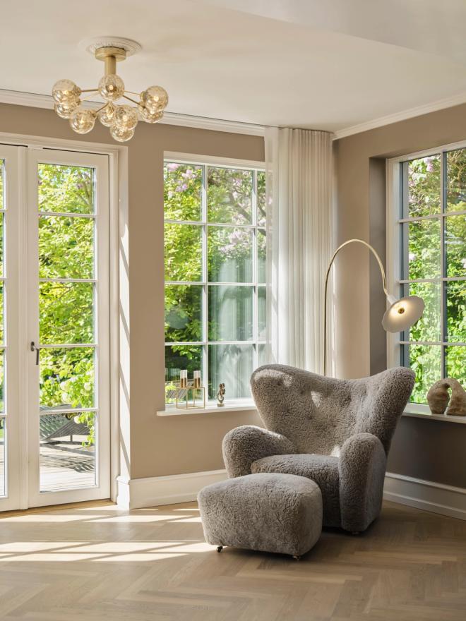  A grey sheepskin armchair, a curved floor lamp, and a chandelier by a door opening onto the garden.