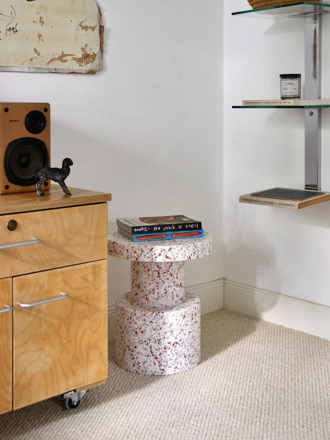 Bit stool holding a stack of books, next to a wooden cabinet with a speaker on top.
