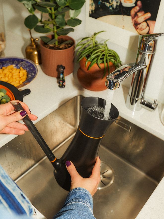 A person is filling a Fiskars watering can under a running faucet