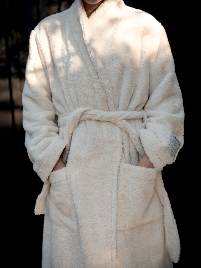 A person wearing an off-white bathrobe with the belt tied at the waist and two large pockets at the front.