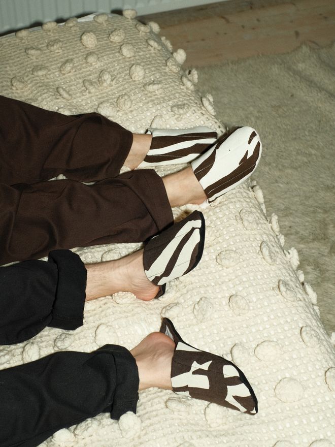 Two people resting their feet on a textured, off-white rug, wearing black-and-white striped slippers