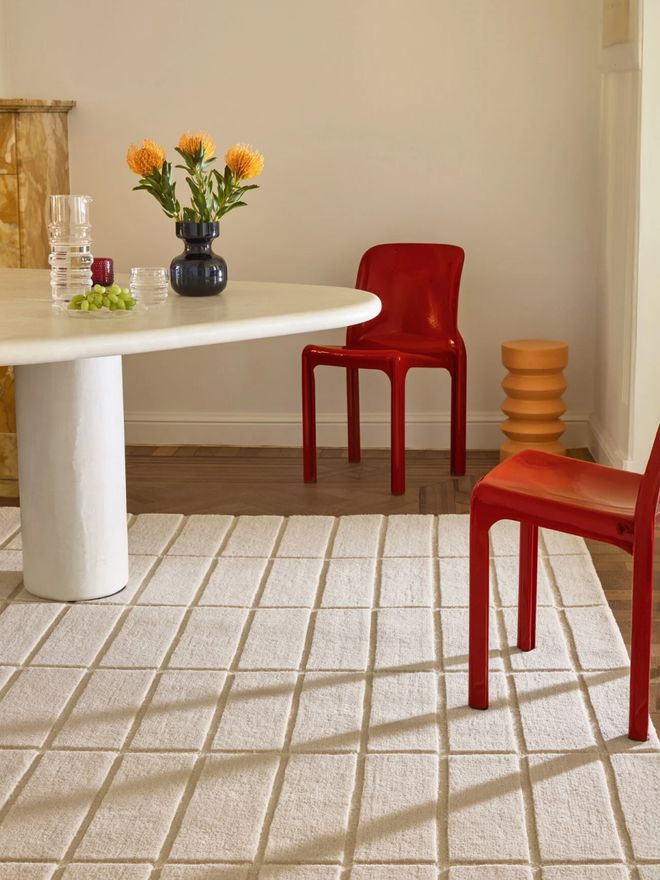 A dining area with Marimekko’s natural white Tiiliskivi wool rug, a round white table and a red chair
