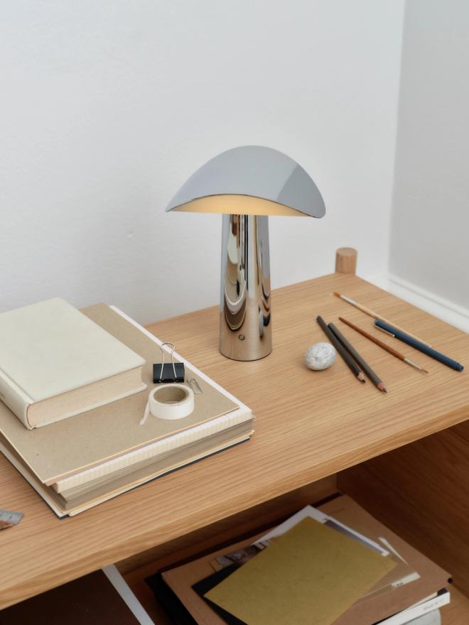 A table lamp with a rounded shade on a desk next to notebooks and pens
