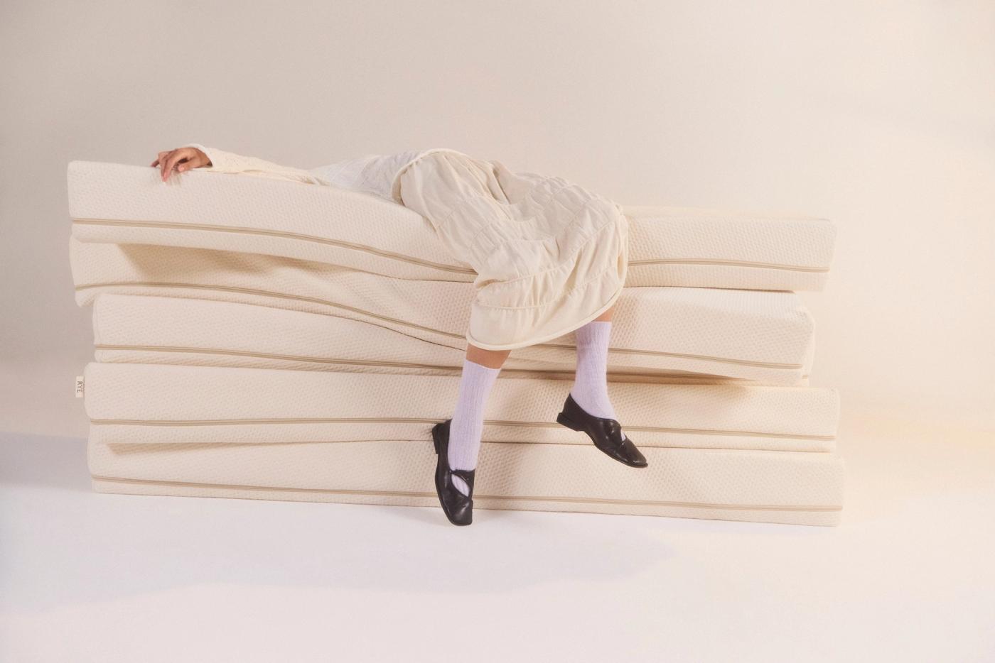 A photo of a woman lying on a pile of mattresses with her legs visible