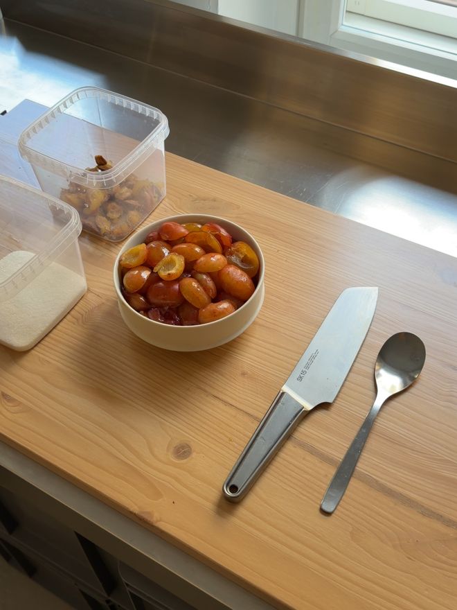 Kulhollinen luumunpuolikkaita, Vearkin Santoku-veitsi ja lusikka puisella työtasolla