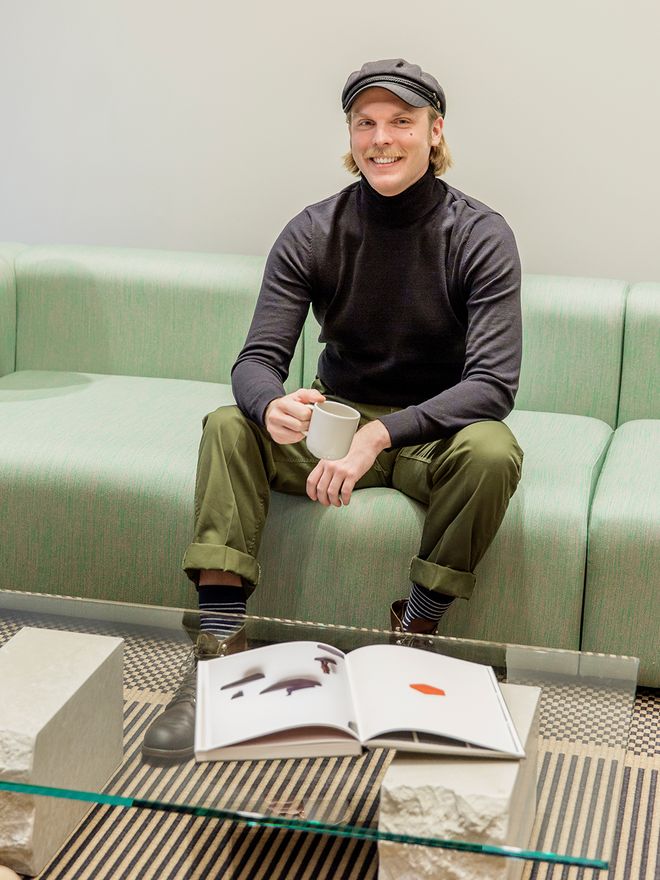 Designmyyjä Matias Rahkola istuu vihreällä sohvalla kahvikuppi kädessään Finnish Design Shopin toimistolla.