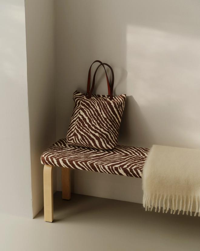 A Zebra-patterned bench in a corner, topped with a matching bag and a pale fringed throw.