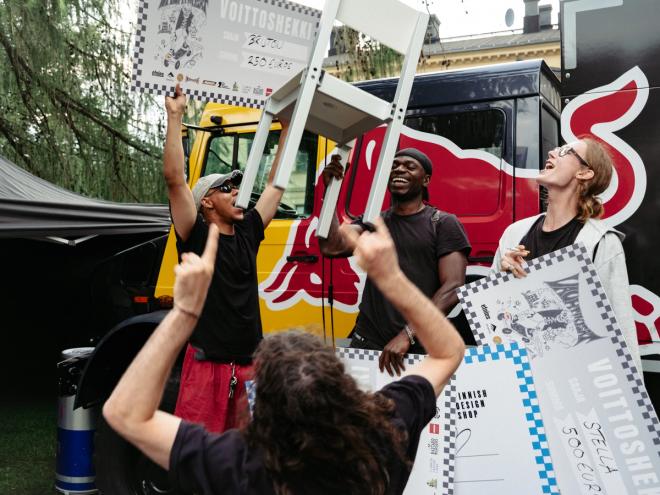 Fredrik Paulsen triumphantly lifts a graphic-printed chair overhead amid a cheering group