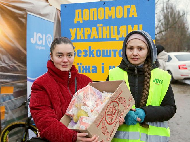 A Ukrainian woman showing a box of supplies and standing next to a JCI volunteer