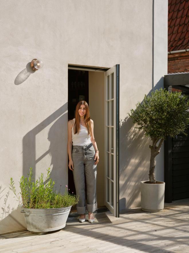 A welcoming portrait of Nadia Lassen standing in the doorway of her bright Frederiksberg villa, inviting guests into a home shaped by family life and Scandinavian light.