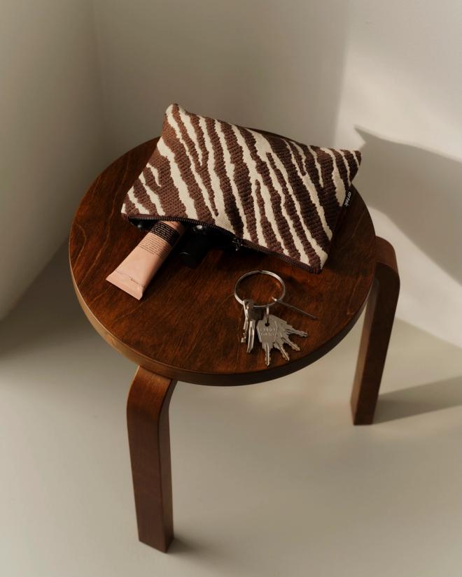 A brown-and-white Zebra-patterned pouch and a set of keys on a dark wooden stool.