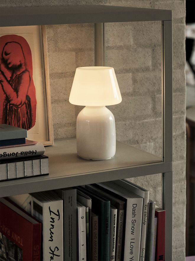 HAY's glass Apollo table lamp shining on a bookshelf.