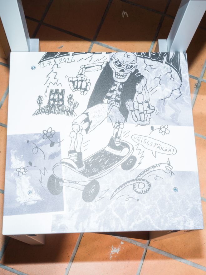 Close-up of the chair seat showing a black-and-white cartoon illustration of a skeleton figure riding a skateboard, with a small house sketch and a handwritten date.