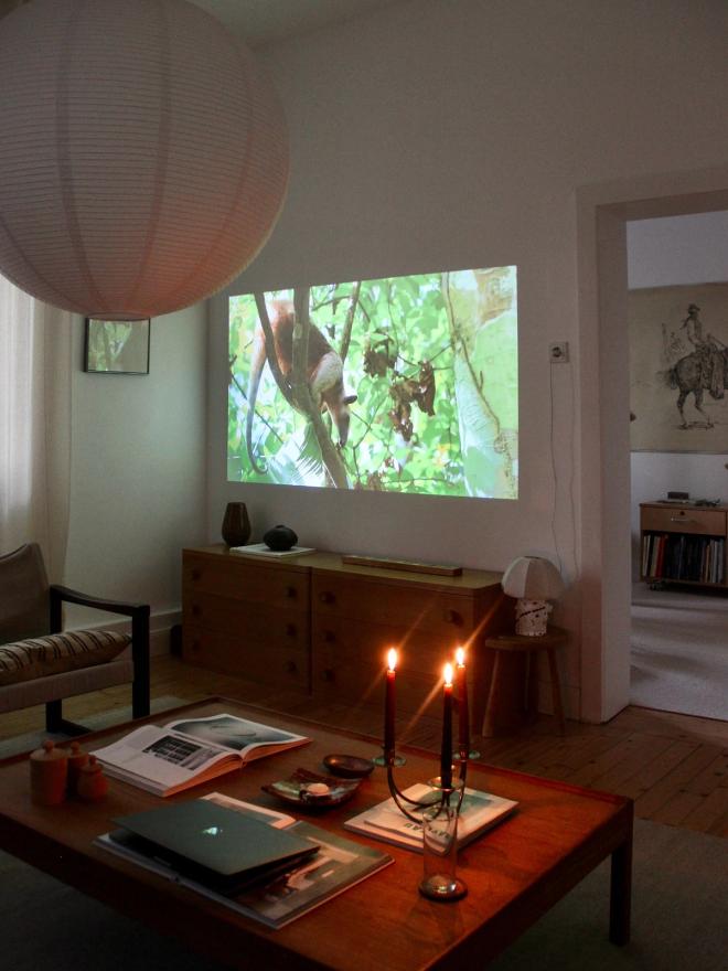 A large round paper pendant lamp in a living room, with a wooden coffee table, lit candles, and a screen on the wall behind.