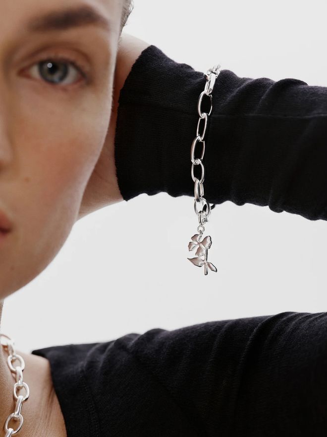 A person holding their hand in front of their face, showing a silver chain bracelet with a small charm