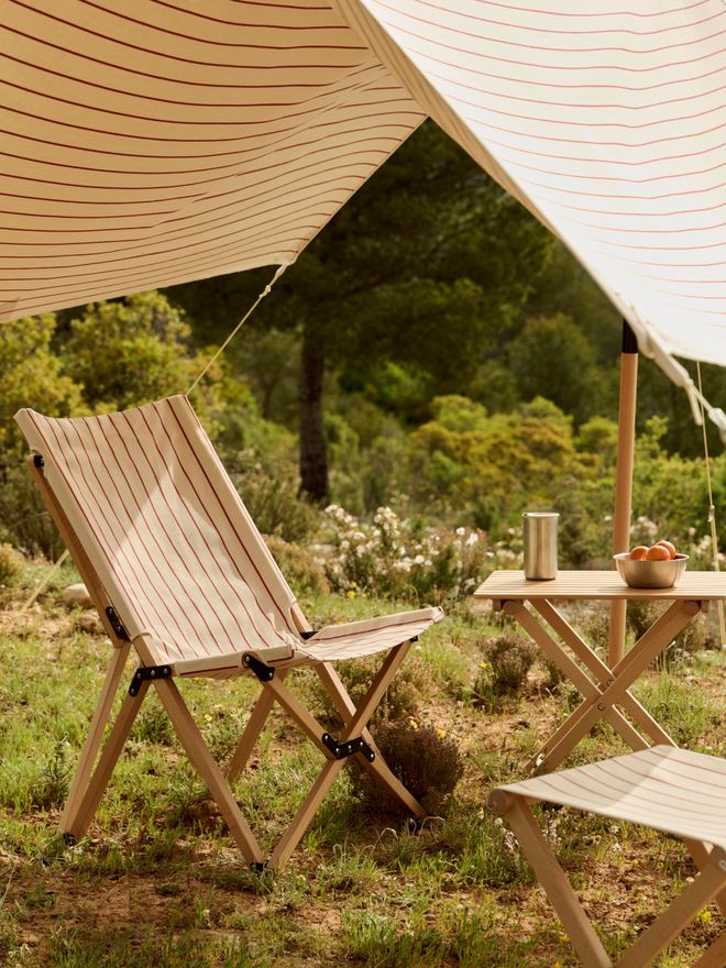 A folding chair and folding table set up under the Outdoor Market canopy in a forest setting