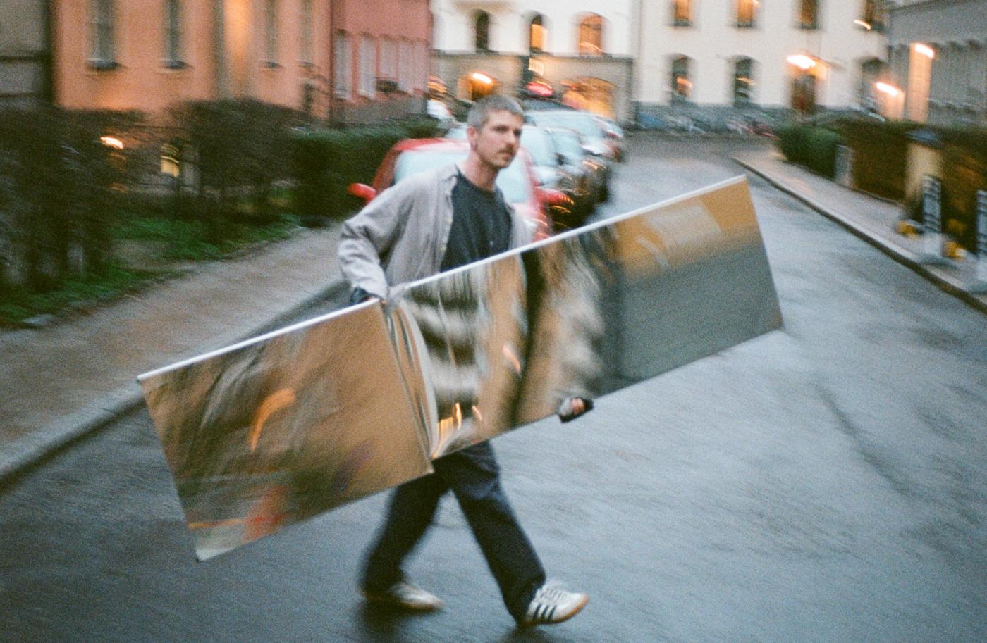 Designer Gustav Winsth walking on the street and carrying his Pleat Mirror for Muuto