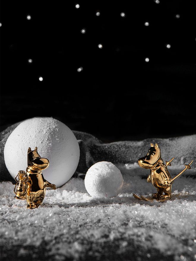 Two gilded Moomintroll figurines in a wintery landscape under a starry night sky.