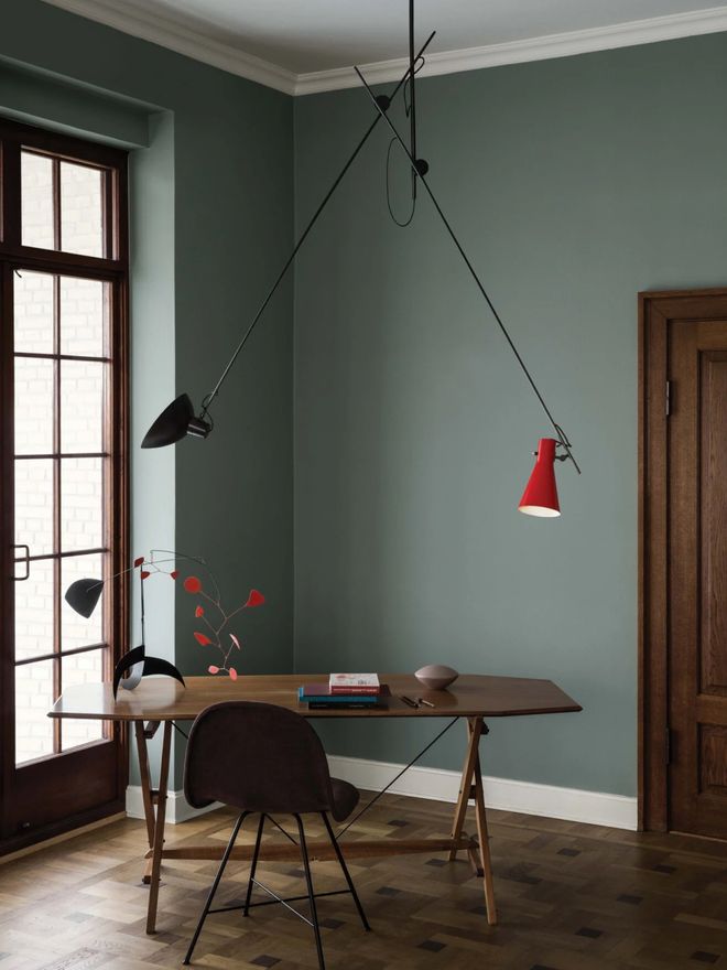 Black and red VV Cinquanta pendant light reaching over a wooden desk with its two arms in a gray-green room.