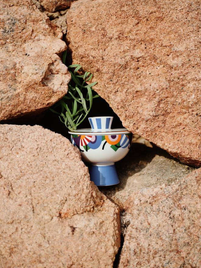 A colourful decorated porcelain jar nestled in the crevice of a boulder