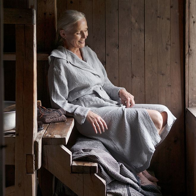 A woman sitting in a sauna wearing the Terva bathrobe by Lapuan Kankurit.
