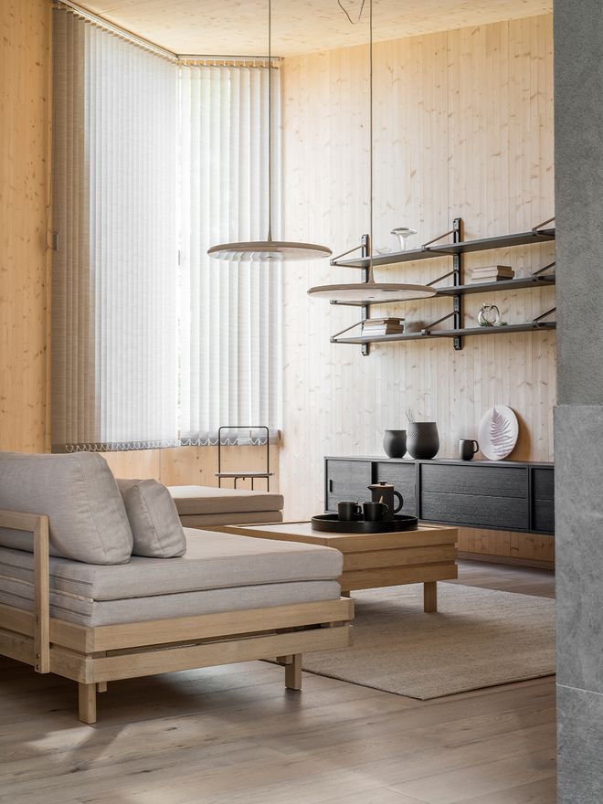 A living room with Tapio Anttila's Day&Night sofa bed and coffee table. In the background, a large shelf unit and a window with blinds on.