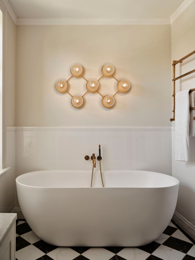 A honeycomb cluster of pearly glass globes above a freestanding tub, set against a black-and-white checkerboard floor