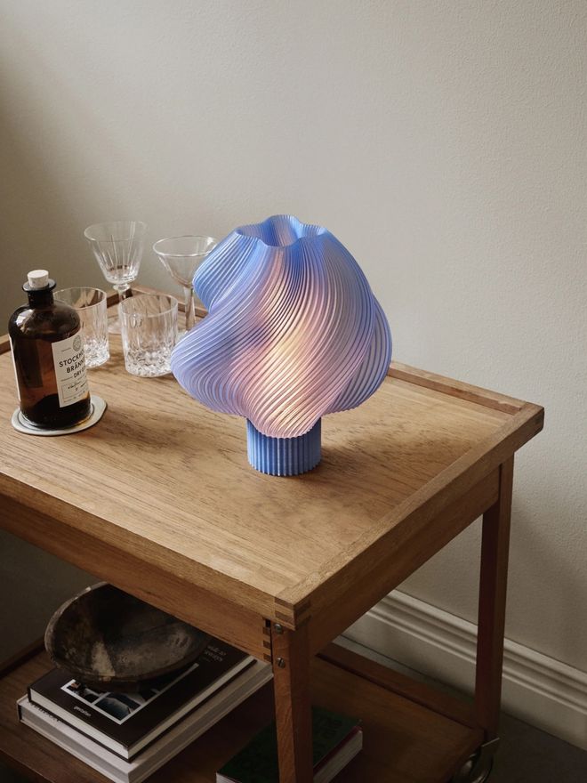 Soft Serve table lamp in the Blueberry Sorbet shade, glowing softly on a side table 