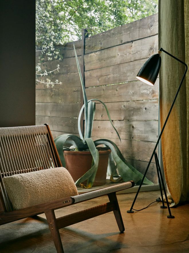 Greta Magnusson Grossman’s black Gröshoppa lamp next to a GUBI armchair