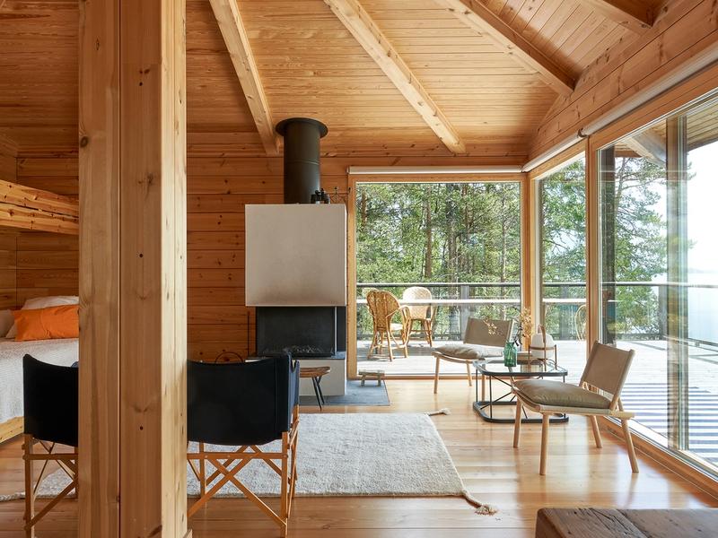The summer cabin's bright living room features the exposed structural framework of the hipped roof, a continuous row of windows facing the lake, and Woodnotes' Uni wool rug on the floor.