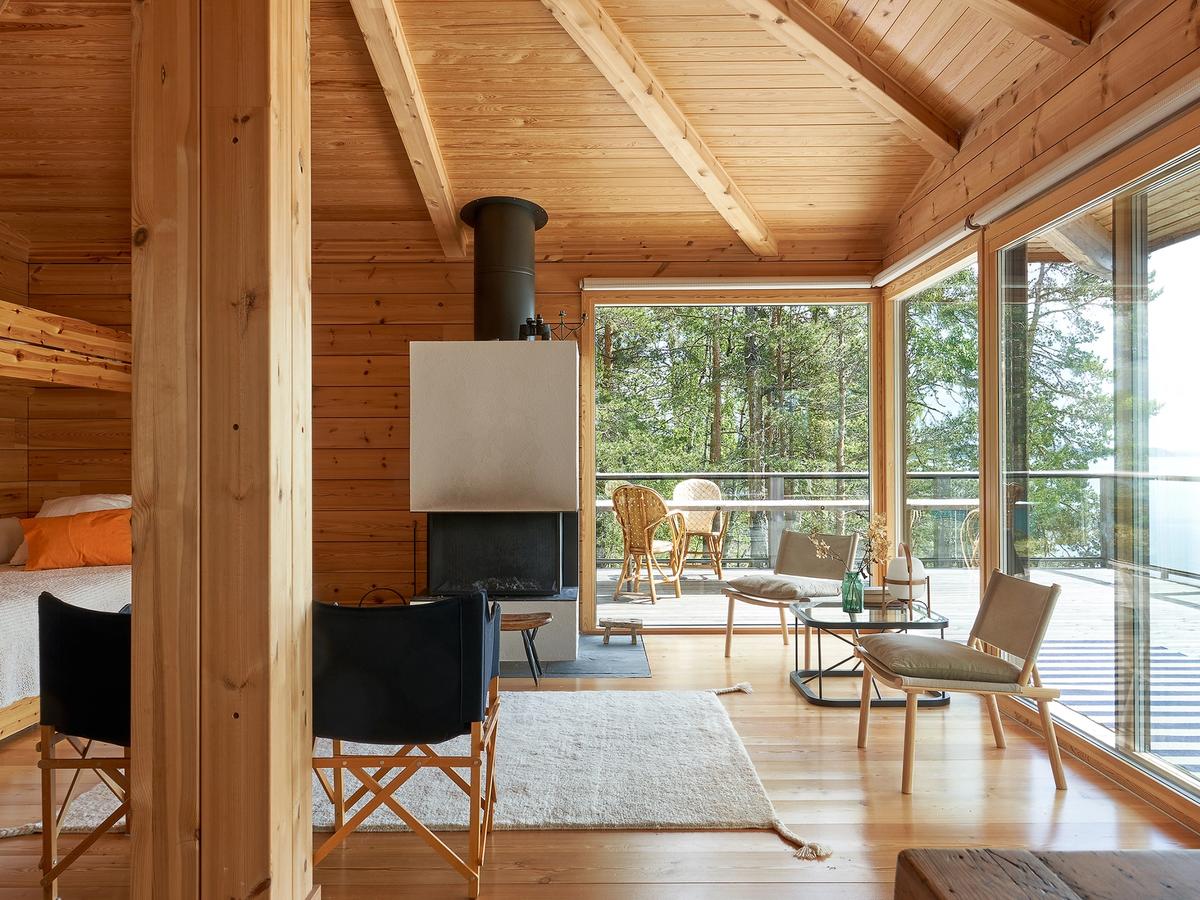 The summer cabin's bright living room features the exposed structural framework of the hipped roof, a continuous row of windows facing the lake, and Woodnotes' Uni wool rug on the floor.
