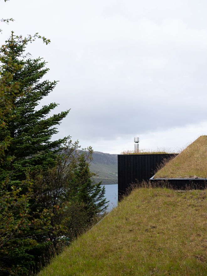 An image of the Holiday home by Þingvallavatn by KRADS architects: a leisure home located in Iceland in the middle of a picturesque scenery. This image features the buildings black facade and a greened roof with moss and grass.