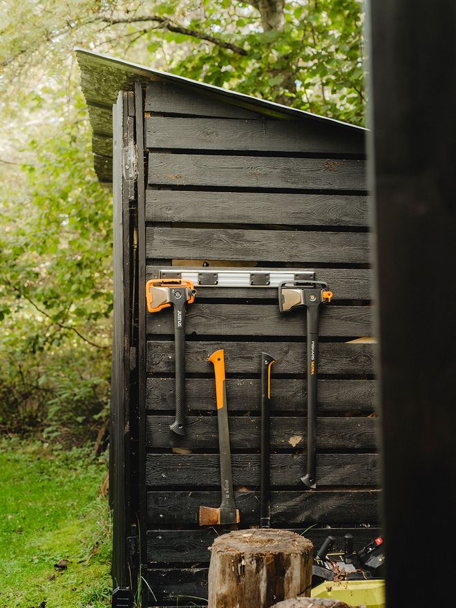 Axes and tools are hung on the exterior wall of a shed