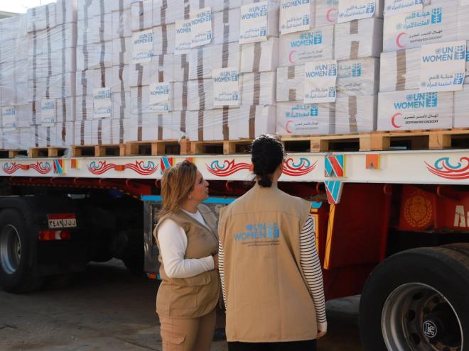Two women observe a truck loaded with aid supplies
