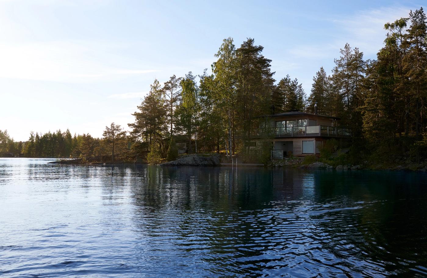A new log cabin right at the shoreline of Lake Saimaa, surrounded by rocks, birches, and pines.