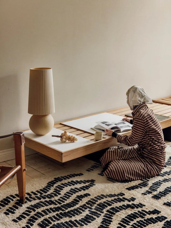 A woman sitting on Saana ja Olli’s beige and black Dyyni rug by a side table