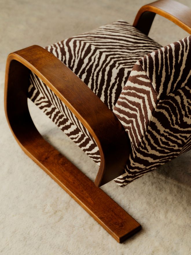 A close-up of the Tankki armchair's curved wooden frame and Zebra-patterned seat on a white shaggy rug.