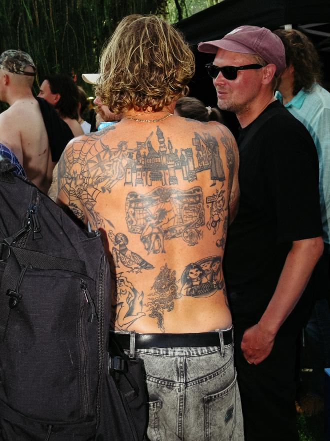A bare, heavily tattooed back is seen from behind in a crowd