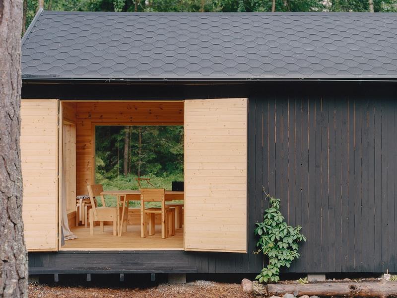 The studio in the archipelago — a black-painted building with its doors open, showing wooden chairs and a dining table inside