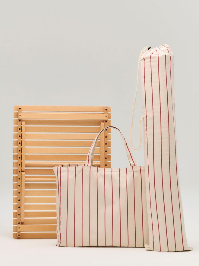 A wooden table folded up, a red-striped canvas bag, and a long storage bag against a light background
