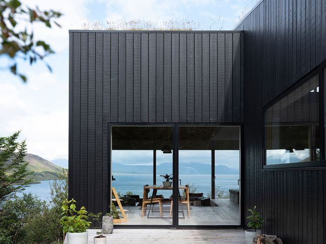 An image of the Holiday home by Þingvallavatn by KRADS architects: a leisure home located in Iceland in the middle of a picturesque scenery. This image features the buildings black facade.