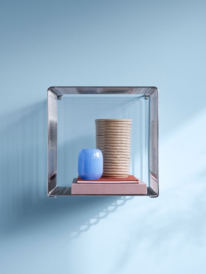 Verner Panton’s modular Wire storage system mounted on a blue wall, styled with books and decorative objects